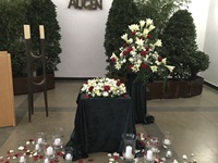 Feierhalle mit Kranz als Urnenschmuck und einem Gesteck in weiß-rot, Kerzen und Rosenblütenblätter